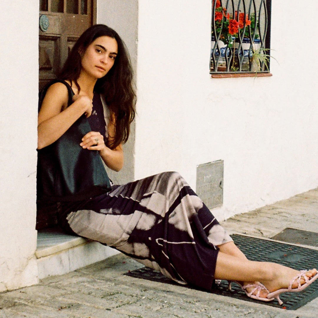 Woman sitting on a ledge in a decorative outdoor setting with plants and flowers.