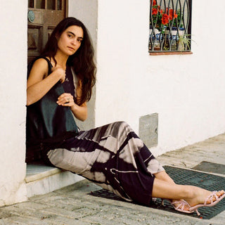 Woman sitting on a ledge in a decorative outdoor setting with plants and flowers.