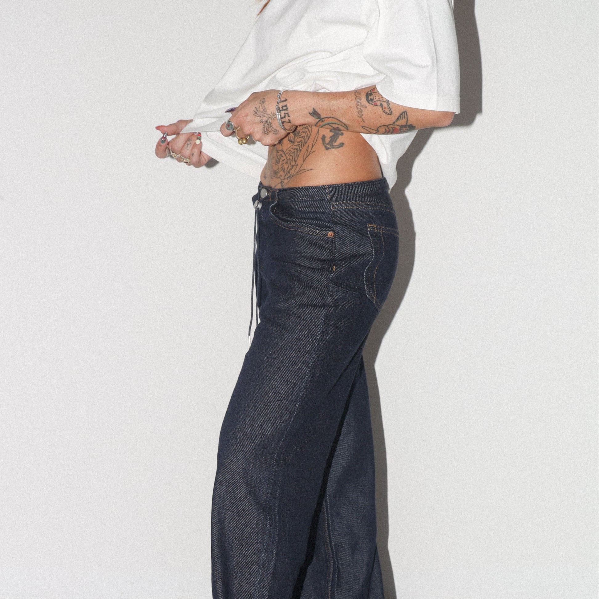 Person wearing a white shirt and dark blue jeans on a plain background