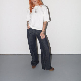 Person wearing a white shirt and dark pants against a plain background