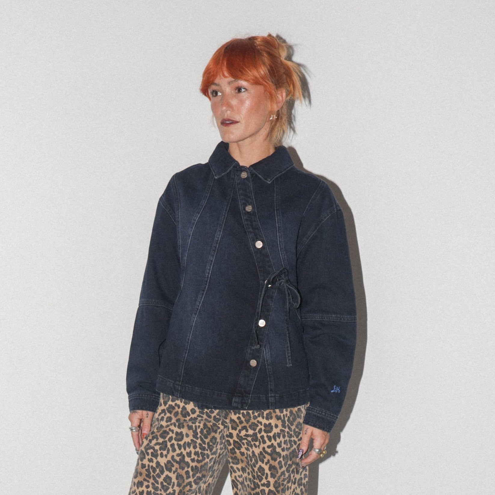 Person wearing a dark denim jacket and leopard print pants against a white background