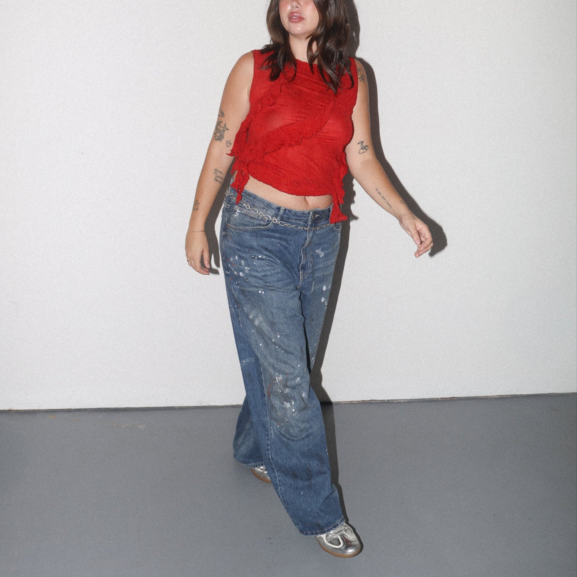 Person wearing a red sleeveless top and blue jeans standing against a plain white background