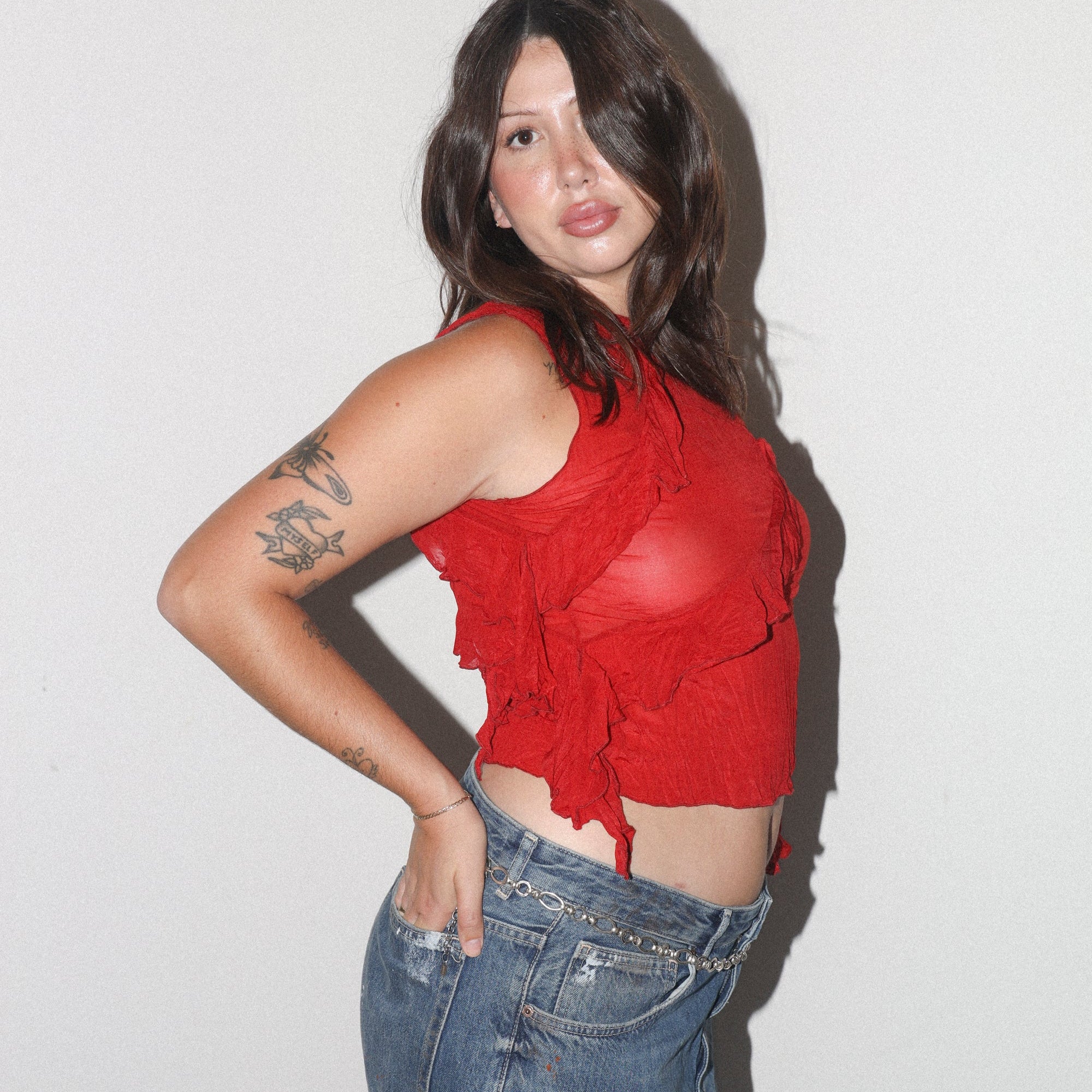 Woman wearing a red top and blue jeans against a plain background