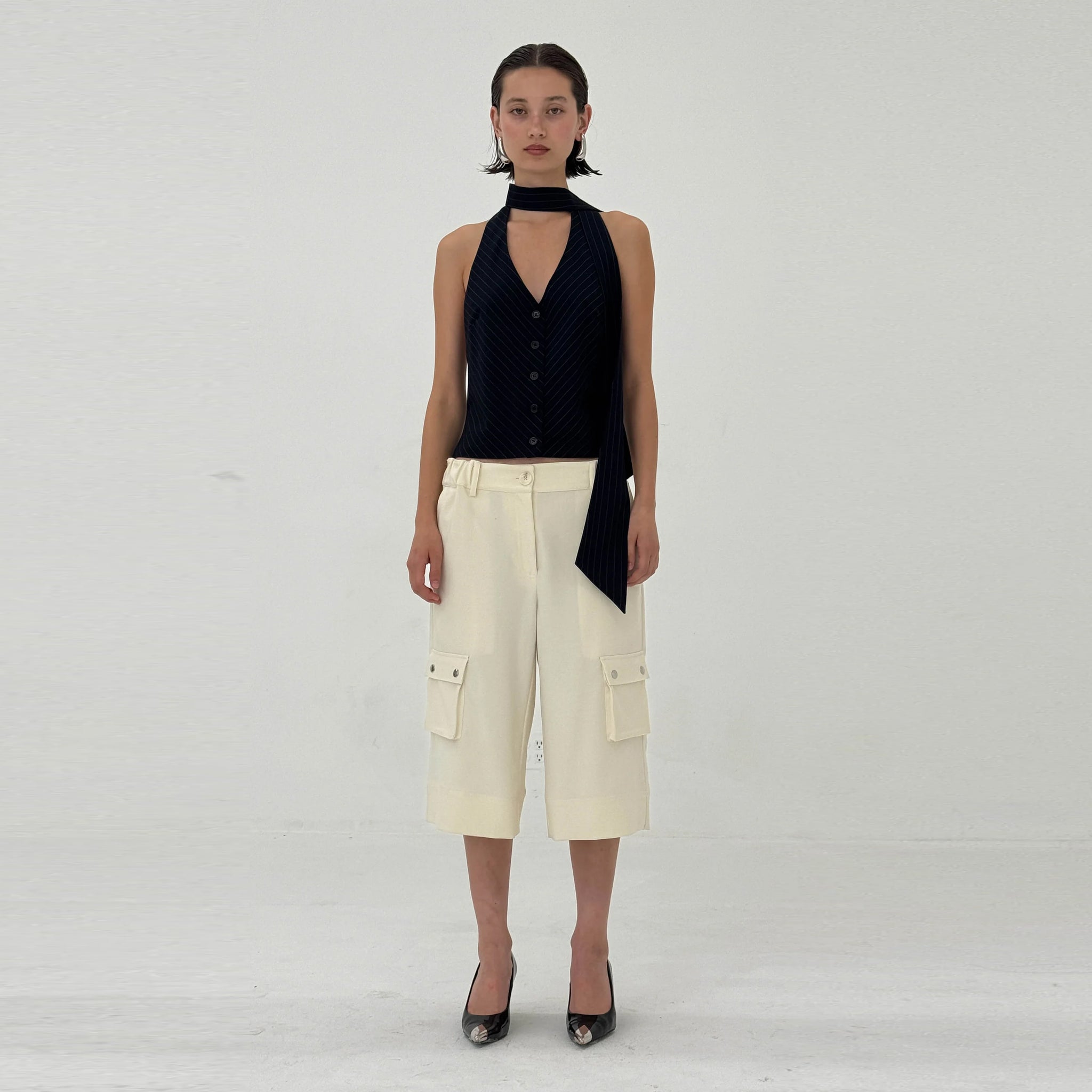 Woman wearing a navy sleeveless top and beige cargo pants on a white background