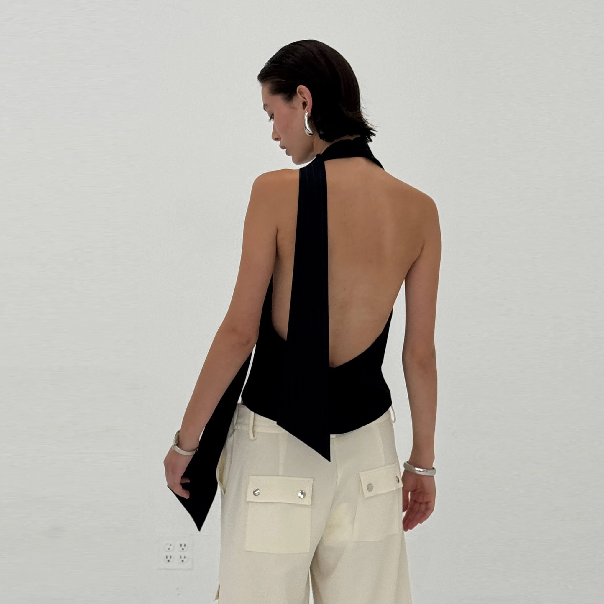 Woman wearing a navy halter top and beige pants against a plain background