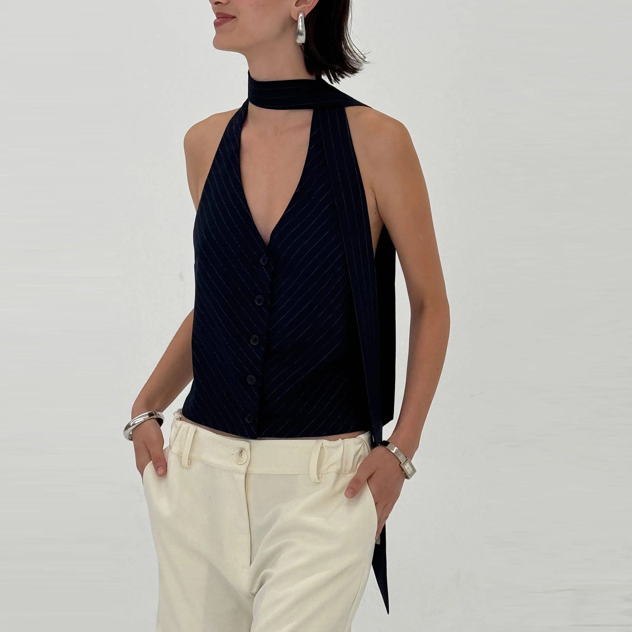 Woman wearing a navy halter neck top and white pants on a plain background