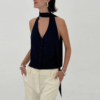 Woman wearing a navy halter neck top and white pants on a plain background