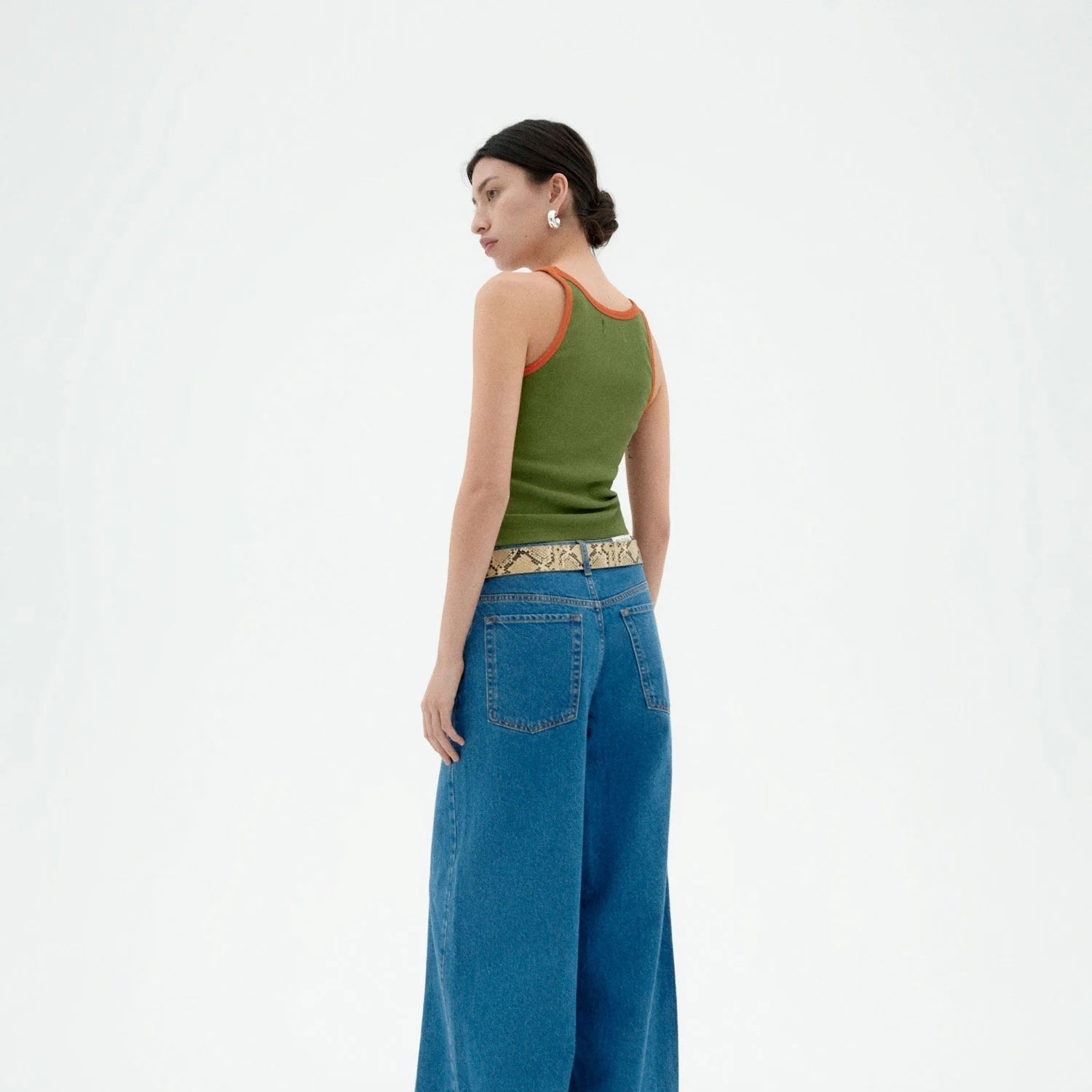 Woman wearing a green tank top and blue jeans on a white background